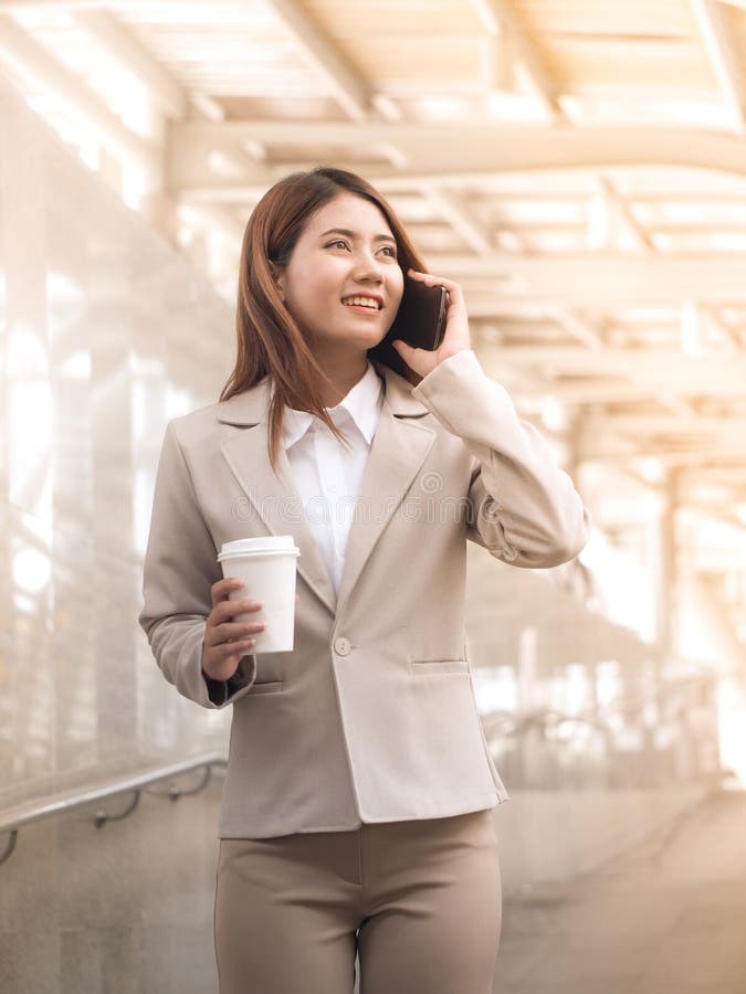 Donna asiatica astuta di affari in un vestito con il telefono cellulare e il holdi fotografia stock Donna asiatica astuta di affari in un vestito con il telefono cellulare e il holdi fotografia stock