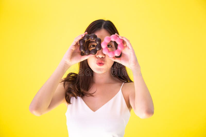 Donna asiatica attraente che tiene due guarnizioni di gomma piuma con l'espressione sorridente sveglia sopra fondo giallo immagine stock Donna asiatica attraente che tiene due guarnizioni di gomma piuma con l'espressione sorridente sveglia sopra fondo giallo immagine stock