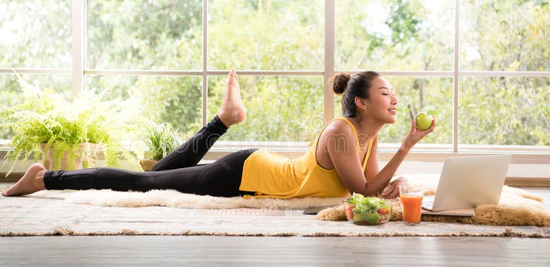 Donna asiatica in buona salute che si trova sul pavimento che mangia insalata che sembra rilassata e comoda