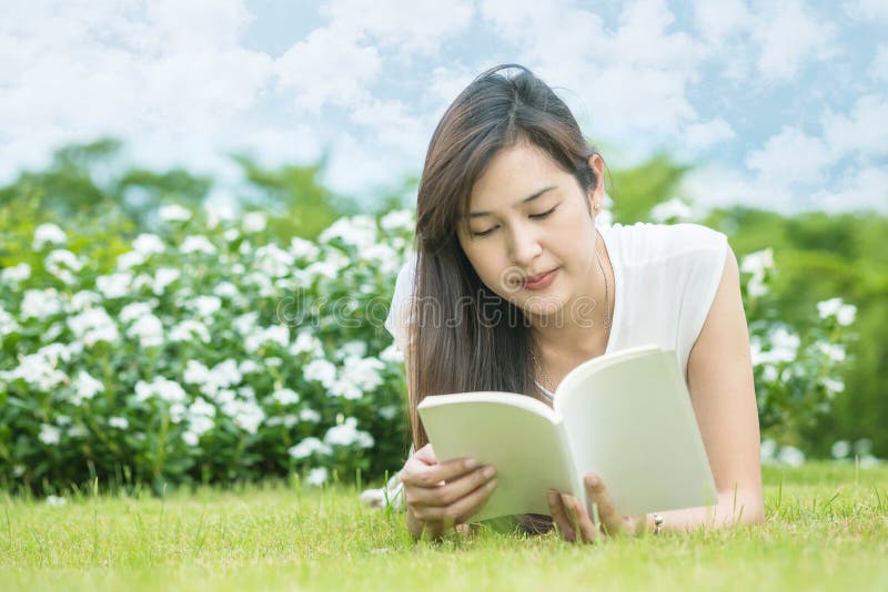 Donna asiatica che si trova sul campo di erba per la lettura del libro bianco nel parco fotografia stock libera da diritti Donna asiatica che si trova sul campo di erba per la lettura del libro bianco nel parco fotografia stock libera da diritti