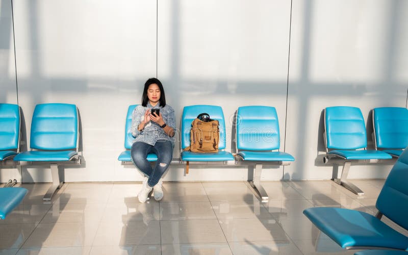 Donna asiatica che usando tempo mobile di uccisione quando aspettano partenza al terminale di aeroporto concetto di corsa immagini stock Donna asiatica che usando tempo mobile di uccisione quando aspettano partenza al terminale di aeroporto concetto di corsa immagini stock