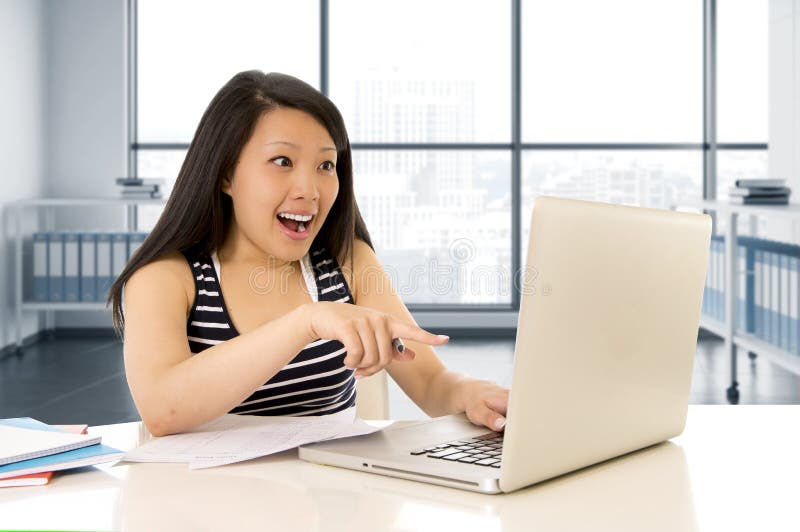 Donna asiatica cinese felice che lavora e che studia sul suo computer che si siede a sorridere moderno della scrivania allegro fotografia stock Donna asiatica cinese felice che lavora e che studia sul suo computer che si siede a sorridere moderno della scrivania allegro fotografia stock
