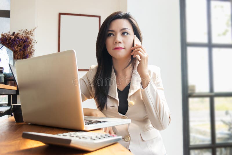 Donna asiatica di affari che lavora con il taccuino del computer portatile ed il cellulare di uso immagine stock libera da diritti Donna asiatica di affari che lavora con il taccuino del computer portatile ed il cellulare di uso immagine stock libera da diritti