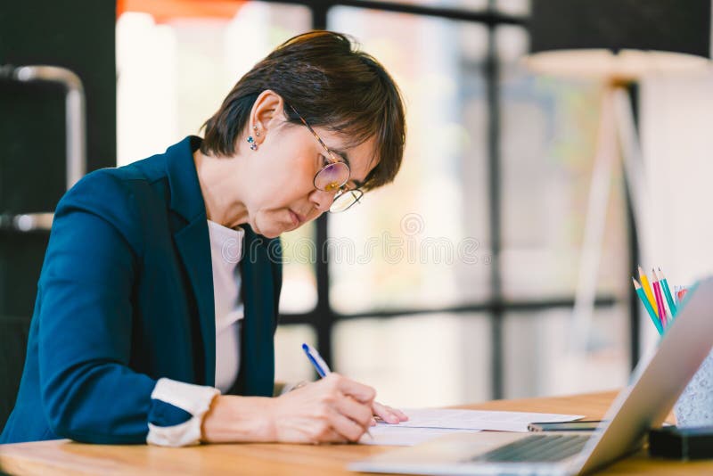 Donna asiatica di medio evo che lavora al lavoro di ufficio in ufficio moderno, con il computer portatile Concetto dell'imprendit fotografie stock Donna asiatica di medio evo che lavora al lavoro di ufficio in ufficio moderno, con il computer portatile Concetto dell'imprendit fotografie stock