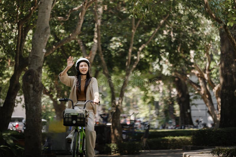 Donna asiatica felice che va in bicicletta in un parco pubblico e che saluta la mano. immagini stock libere da diritti