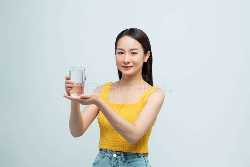 Donna asiatica sorride beve un bicchiere d'acqua felice in una stanza bianca immagine stock libera da diritti
