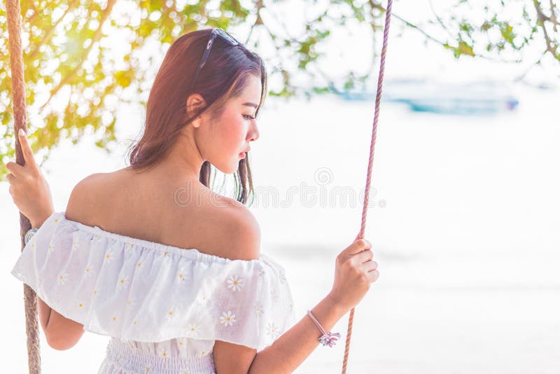 Donna asiatica sul vestito bianco che si siede sull'oscillazione alla spiaggia La gente e immagine stock libera da diritti Donna asiatica sul vestito bianco che si siede sull'oscillazione alla spiaggia La gente e immagine stock libera da diritti