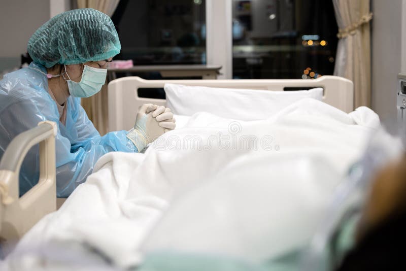 Donna asiatica triste o infermiera mascherata e uniforme medica pregano con gli occhi chiusi, aggrappati insieme, dicono una pregh immagini stock