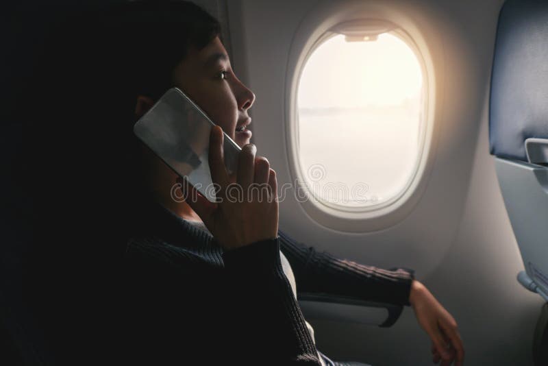 Donna asiatica turistica che si siede vicino alla finestra dell'aeroplano e che per mezzo dello Smart Phone durante il volo immagini stock Donna asiatica turistica che si siede vicino alla finestra dell'aeroplano e che per mezzo dello Smart Phone durante il volo immagini stock
