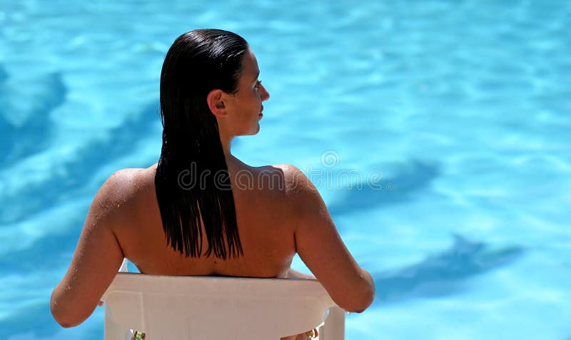 Donna attraente che si siede dalla piscina piena di sole blu fotografia stock libera da diritti