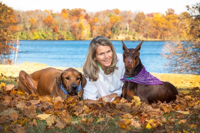 Donna attraente di medio evo che si rilassa nel lago con i suoi 2 grandi cani di animale domestico fotografia stock Donna attraente di medio evo che si rilassa nel lago con i suoi 2 grandi cani di animale domestico fotografia stock