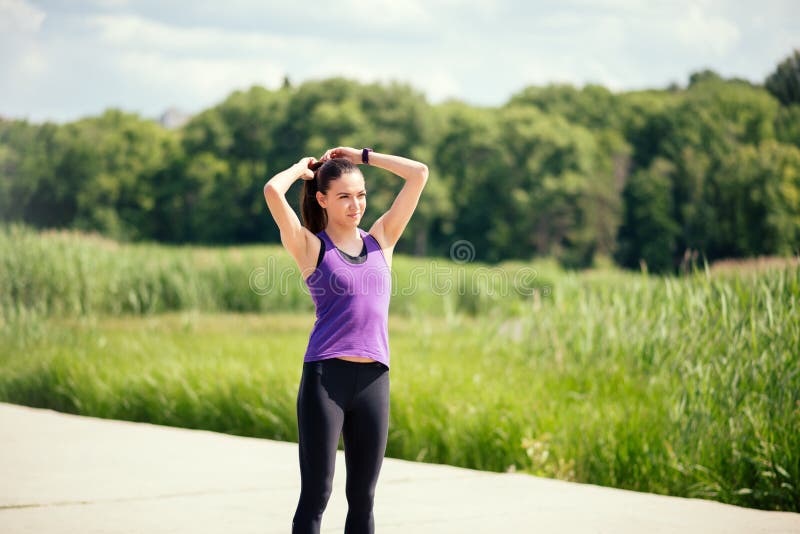 Donna attraente sportiva fare una coda e una ricreazione prima o dopo l'allenamento e un funzionamento di cavallino sul fondo del fotografia stock Donna attraente sportiva fare una coda e una ricreazione prima o dopo l'allenamento e un funzionamento di cavallino sul fondo del fotografia stock