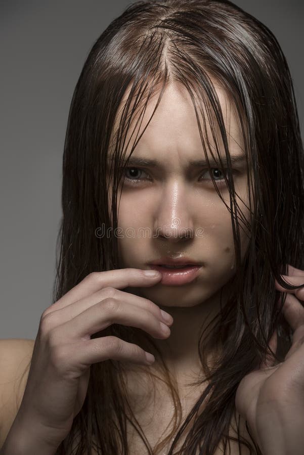 Close-up portrait of young girl with clean skin, long wet hair and some water drops on the face. Looking in camera with angry expression. Close-up portrait of young girl with clean skin, long wet hair and some water drops on the face. Looking in camera with angry expression