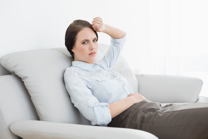 Donna ben vestito seria che si siede sul sofà immagine stock libera da diritti Donna ben vestito seria che si siede sul sofà immagine stock libera da diritti