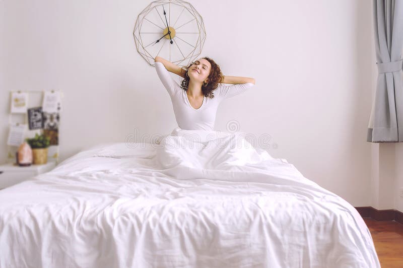 Donna bionda che si siede vicino alla grande finestra bianca mentre allungando sul letto fotografie stock libere da diritti Donna bionda che si siede vicino alla grande finestra bianca mentre allungando sul letto fotografie stock libere da diritti