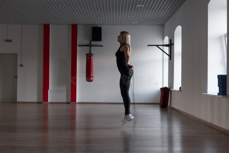 Donna bionda esile giovane che fa gli esercizi con un salto della corda in una palestra Ragazza di sport in un salto Cardio addes fotografia stock Donna bionda esile giovane che fa gli esercizi con un salto della corda in una palestra Ragazza di sport in un salto Cardio addes fotografia stock