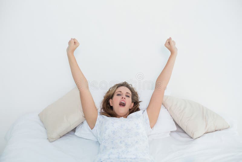 Donna bionda graziosa che allunga a letto e che sbadiglia immagini stock libere da diritti Donna bionda graziosa che allunga a letto e che sbadiglia immagini stock libere da diritti