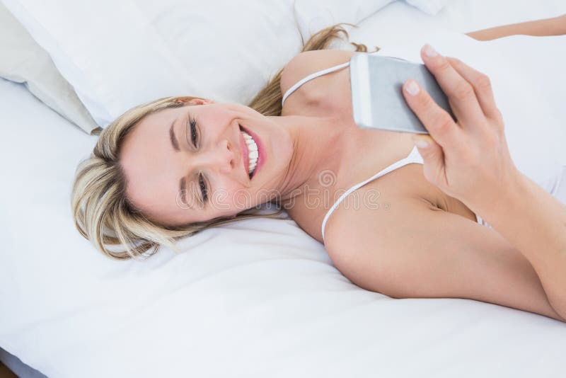 Donna bionda sorridente che si trova a letto invio di messaggi di testo fotografia stock libera da diritti Donna bionda sorridente che si trova a letto invio di messaggi di testo fotografia stock libera da diritti