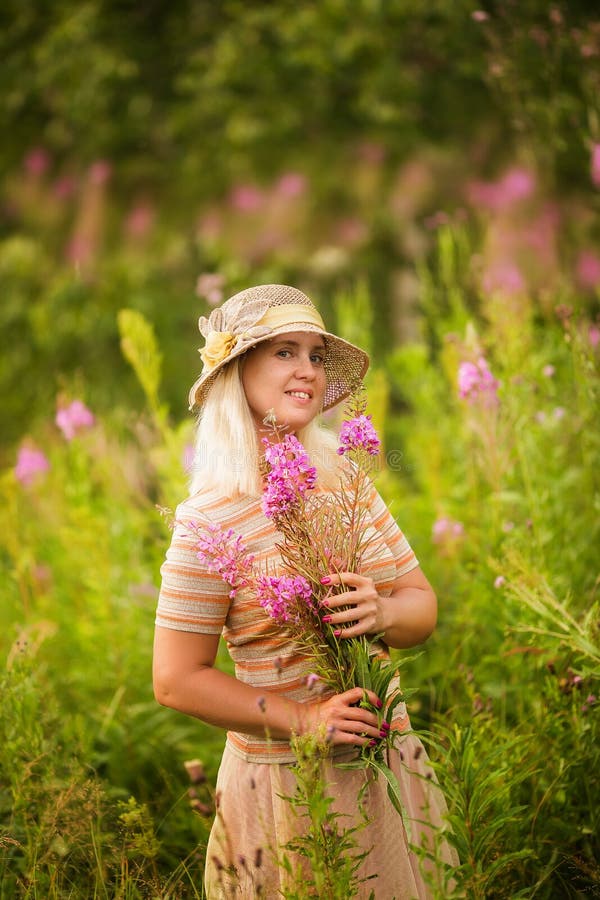 Donna bionda sorridente sveglia con i wildflowers Ritratto di estate di una donna con rosa-tè nel campo fotografia stock libera da diritti Donna bionda sorridente sveglia con i wildflowers Ritratto di estate di una donna con rosa-tè nel campo fotografia stock libera da diritti
