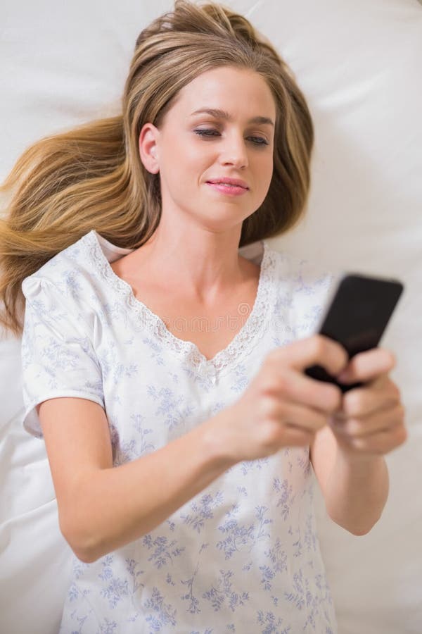 Donna calma naturale che si trova sul letto facendo uso dello smartphone fotografia stock Donna calma naturale che si trova sul letto facendo uso dello smartphone fotografia stock