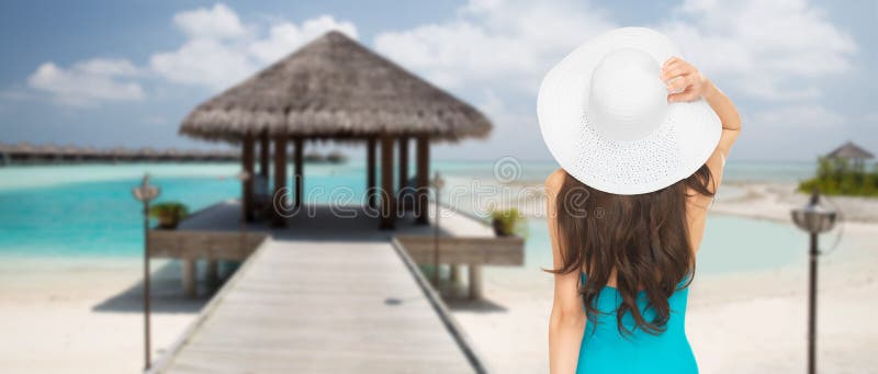 Donna in cappello del sole e del costume da bagno dalla parte posteriore sulla spiaggia