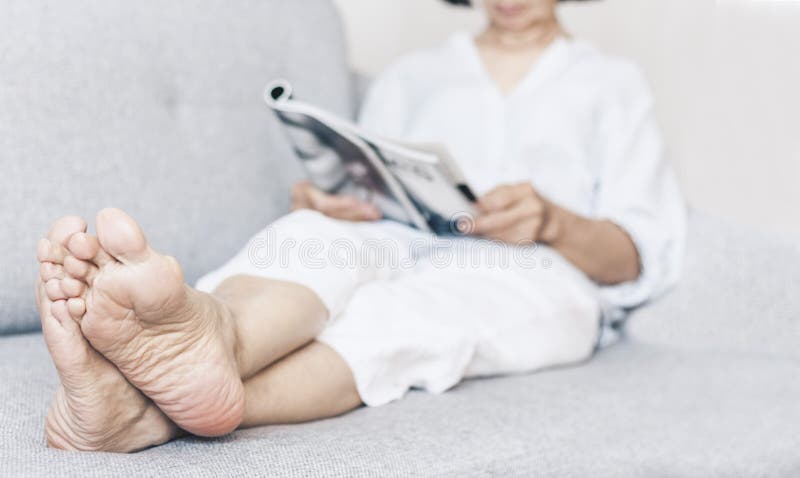 Donna castana di mezza et? con i vetri sulla rivista grigia della lettura del sof? immagini stock libere da diritti Donna castana di mezza et? con i vetri sulla rivista grigia della lettura del sof? immagini stock libere da diritti