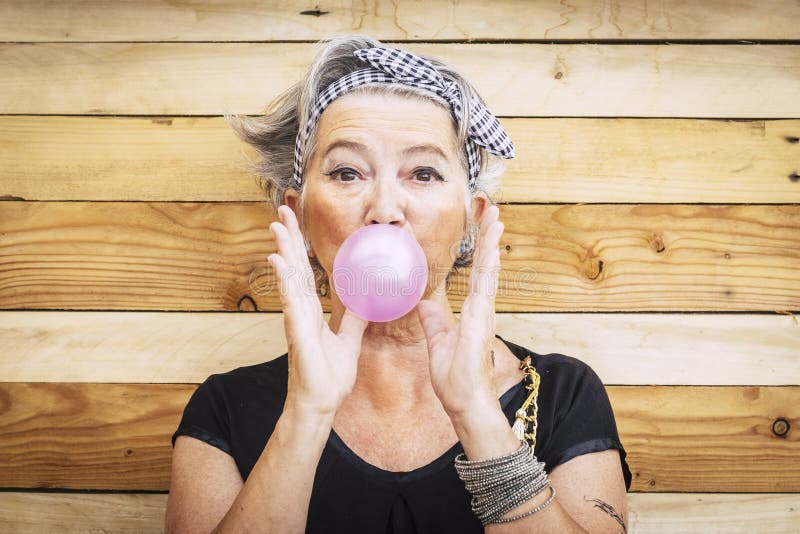 Donna caucasica divertente ed alternativa della gente anziana bella con la gomma da masticare della bolla rosa - ritratto di sign