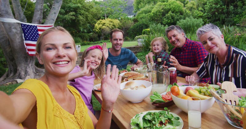 Donna caucasica sorridente che si fa il selfie con una famiglia di tre generazioni che cena in giardino