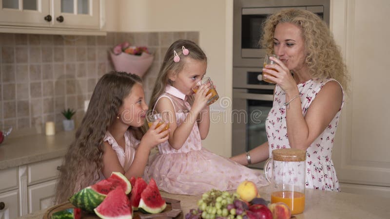 Donna caucasica sorridente e ragazze che portano bicchieri di succo bevendo una bevanda di vitamina saporita al mattino. ritratto archivi video