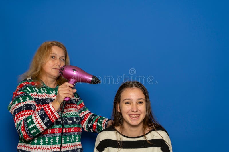 Donna caucasica sui 40 anni asciugando i capelli delle figlie adolescenti isolata su sfondo blu. immagini stock