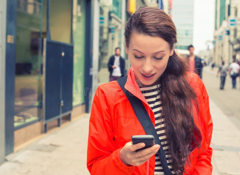 Donna che cammina su una via della città e che per mezzo del suo telefono cellulare fotografia stock Donna che cammina su una via della città e che per mezzo del suo telefono cellulare fotografia stock