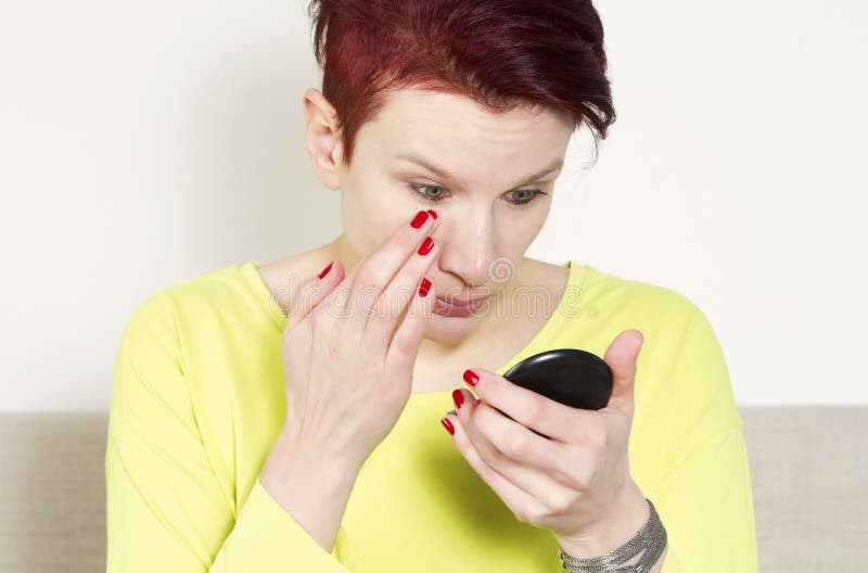 Donna che controlla il suo trucco in piccolo specchio fotografia stock Donna che controlla il suo trucco in piccolo specchio fotografia stock