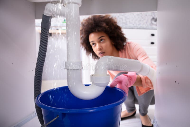 Portrait Of An Young African Woman Looking At Water Leaking From Sink Pipe. Portrait Of An Young African Woman Looking At Water Leaking From Sink Pipe