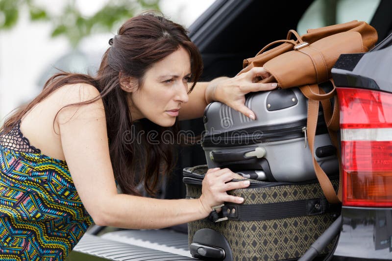 Donna che fatica a portare i bagagli nel bagagliaio dell'auto fotografia stock