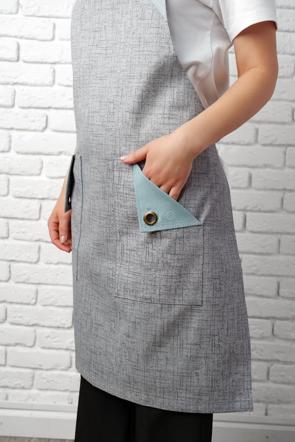 Donna che indossa un grembiule grigio con una camicia bianca davanti a un muro di mattoni bianchi immagini stock libere da diritti