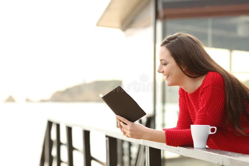 Side view of happy woman wearing a red sweater reading an ebook in an hotel or apartment on the beach on holidays. Side view of happy woman wearing a red sweater reading an ebook in an hotel or apartment on the beach on holidays