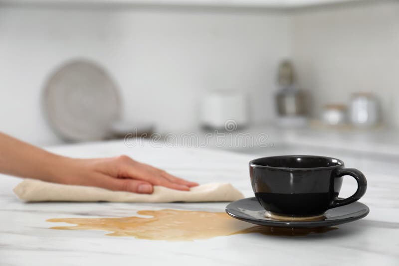 Donna che pulisce il caffè versato sul tavolo di marmo bianco in cucina. spazio per il testo fotografia stock libera da diritti