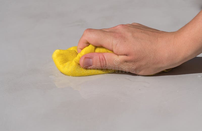 Donna che pulisce a mano l'acqua rovesciata su un pavimento di cemento con un panno di stoffa giallo per pavimenti fotografie stock