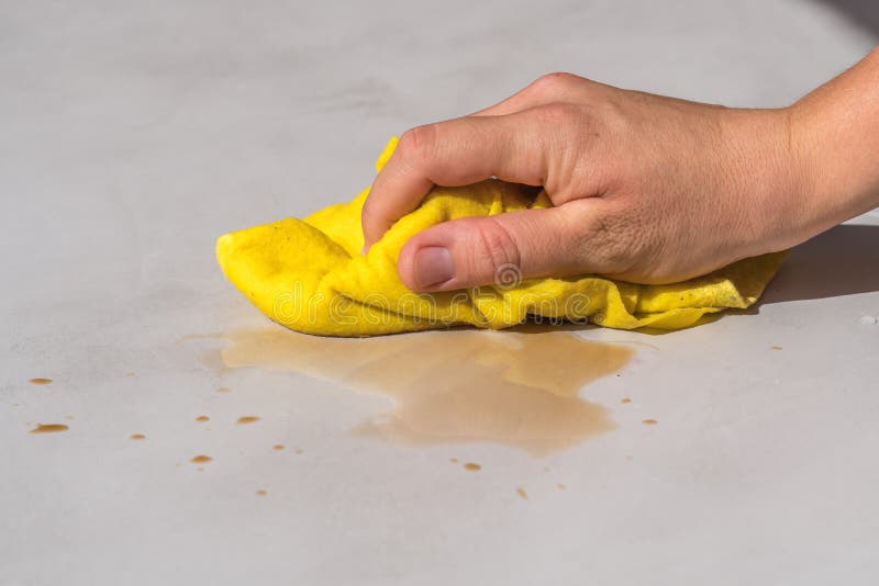 Donna che pulisce a mano l'acqua rovesciata su un pavimento di cemento con un panno di stoffa giallo per pavimenti fotografia stock
