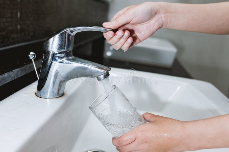 Donna che riempie un bicchiere d'acqua da un acciaio inossidabile o da un cromo immagine stock Donna che riempie un bicchiere d'acqua da un acciaio inossidabile o da un cromo immagine stock