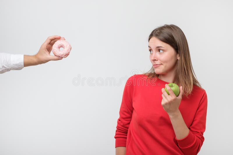 Dieting or good health concept. Young woman rejecting unhealthy food such as donut or dessert and choosing healthy food such as fresh fruit or vegetable. Dieting or good health concept. Young woman rejecting unhealthy food such as donut or dessert and choosing healthy food such as fresh fruit or vegetable