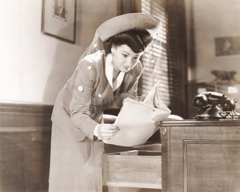 Donna che rubacchia uno sguardo ai documenti in ufficio immagine stock libera da diritti Donna che rubacchia uno sguardo ai documenti in ufficio immagine stock libera da diritti