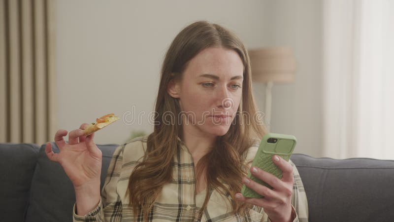 Donna che scrive messaggi su smartphone e mangia pizza video d archivio