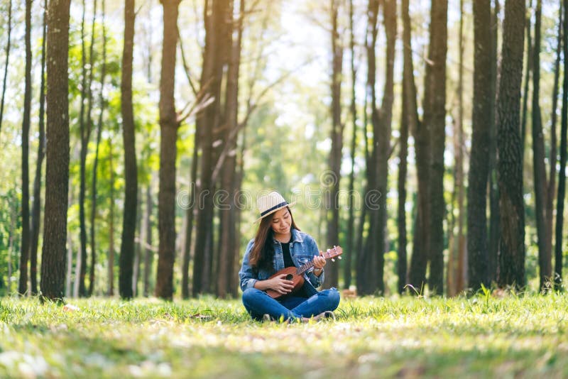 Donna che si siede e che gioca ukulele nell'aria aperta immagine stock Donna che si siede e che gioca ukulele nell'aria aperta immagine stock
