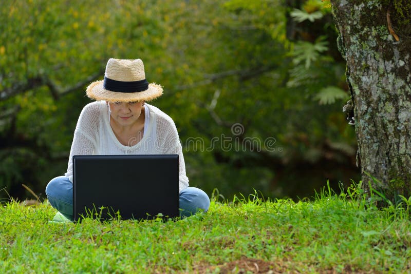 Donna che si siede sull'erba verde facendo uso del computer portatile fotografia stock Donna che si siede sull'erba verde facendo uso del computer portatile fotografia stock