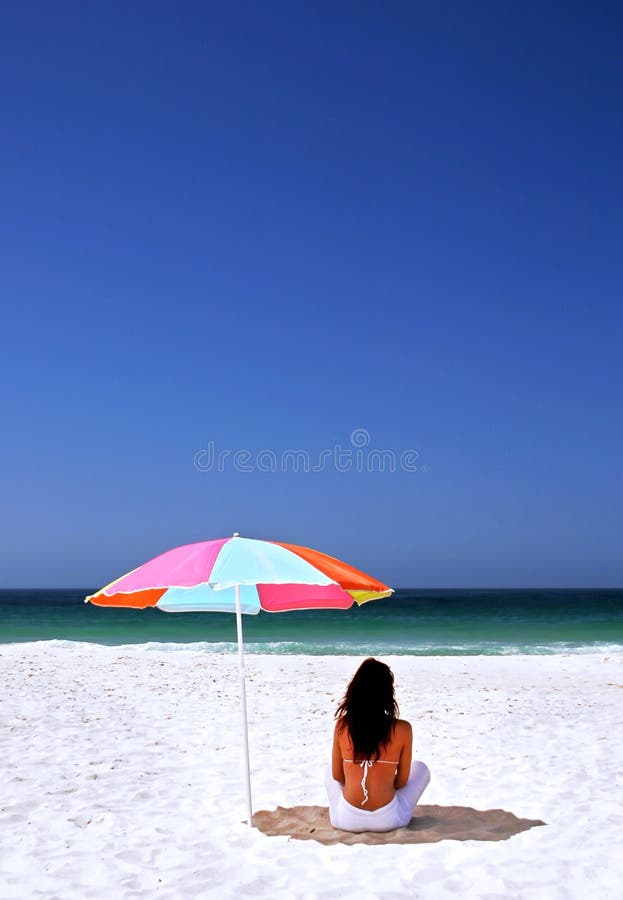 Donna che si siede sulla spiaggia spagnola sotto l'ombrello di sole. Mare blu e cielo della sabbia bianca. fotografie stock libere da diritti