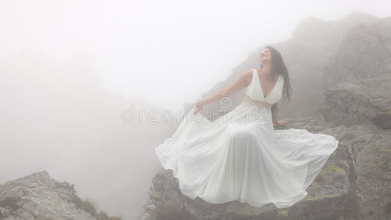 Donna che si siede sulle rocce in nebbia immagine stock Donna che si siede sulle rocce in nebbia immagine stock