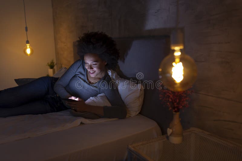 Beautiful young mixed race woman lying in bed and using a smartphone. Beautiful young mixed race woman lying in bed and using a smartphone