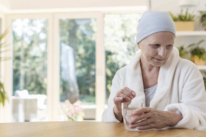 Donna che soffrono dall'accappatoio d'uso del cancro ovarico e foulard che prende le pillole a casa immagine stock Donna che soffrono dall'accappatoio d'uso del cancro ovarico e foulard che prende le pillole a casa immagine stock