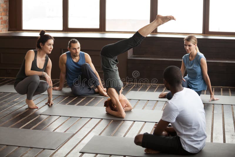 Donna che sta sull'yoga di pratica della testa al corso di formazione del gruppo immagine stock libera da diritti Donna che sta sull'yoga di pratica della testa al corso di formazione del gruppo immagine stock libera da diritti